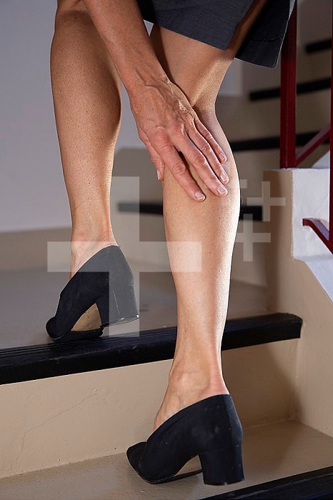 Close-up of a woman’s legs. She is climbing stairs and has a hand on her calf.