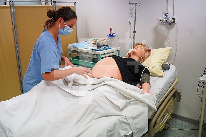 Students facing a post natal emergency follow procedures on a mannequin. This dummy is controlled by operators in an adjoining room. Here, a woman with heavy bleeding following a home birth.