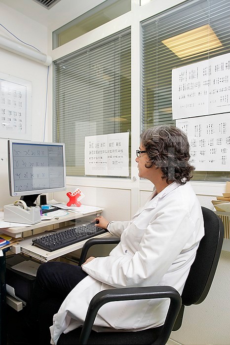 Cytogenetics laboratory, surrounded by karyotypes, a doctor analyzes the results of a sample in order to write a report.