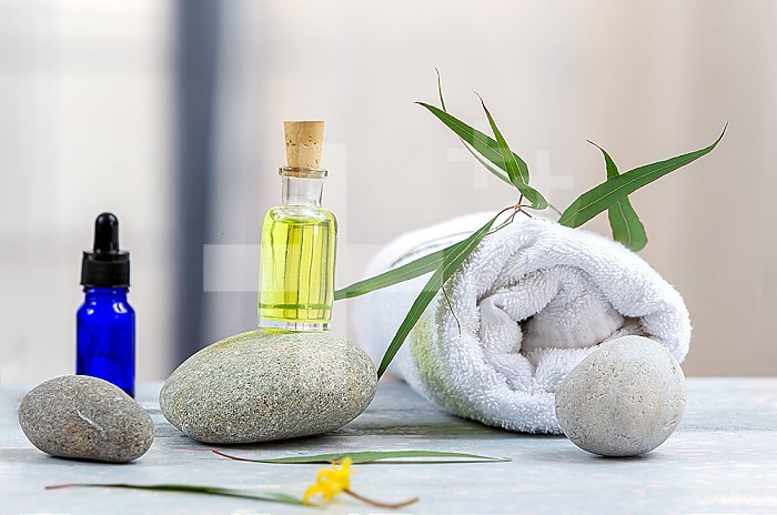 Bottles of essential oils, pebbles and bath towel in a bathroom.