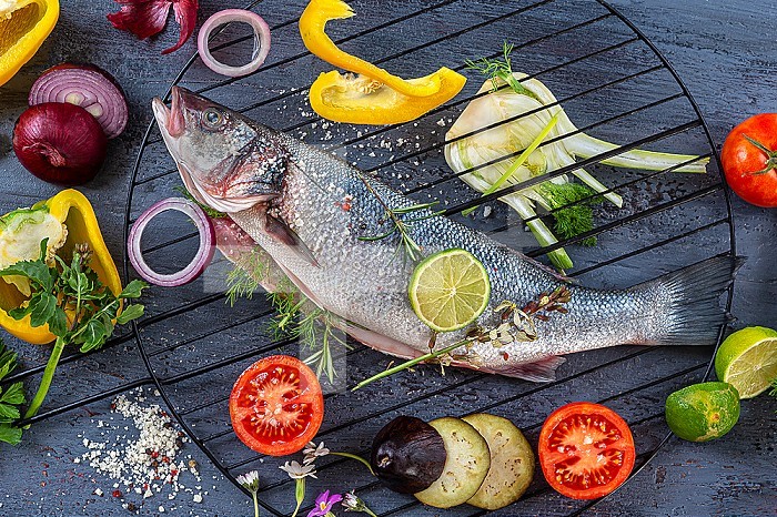 Sea bass placed on a barbecue grill surrounded by vegetables, before cooking.