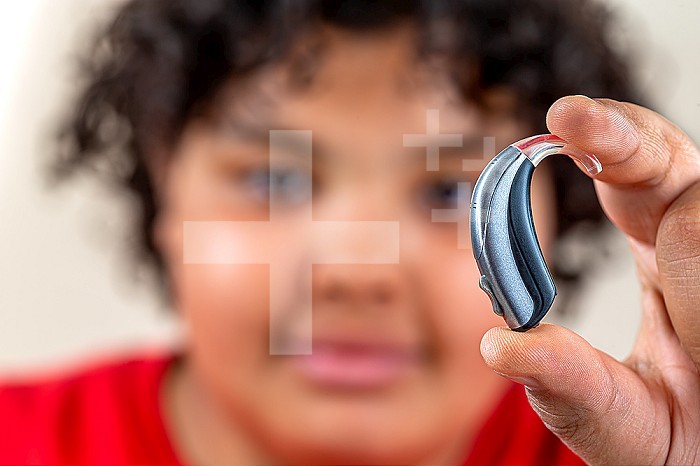 14 year old boy holding a hearing aid.