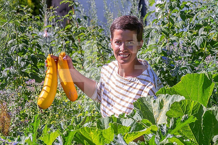 Young woman holding up two beautiful yellow zucchinis