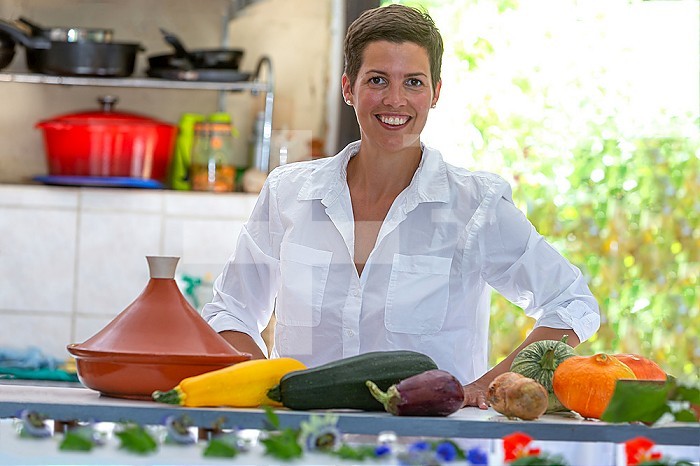Young smiling woman behind a worktop supporting vegetables from the vegetable garden for the tagine.