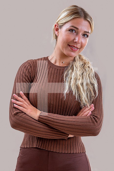 Smiling 26 year old woman with arms crossed against gray background.