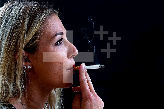 Close-up of a young woman smoking a cigarette against a black background, creating billows of smoke.