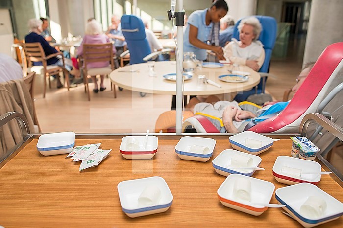 EHPAD - Residents having their meal in the common room. Serving tray with bowls filled with petit suisses.