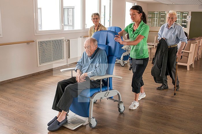 EHPAD - Deaf nurse pushing an elderly disabled resident in a wheelchair and accompanying deaf residents in the dining hall.
