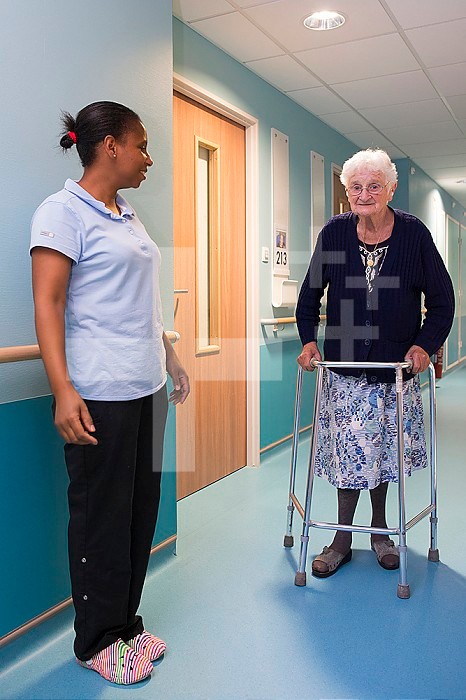 EHPAD - Caregiver encouraging a resident to move around alone with the help of a walker in a hallway.