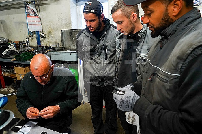 Business immersion of five workers from the mechanical workshop of an ESAT. Under the responsibility of auto mechanic professionals, workers with disabilities are trained in the mechanical profession and work independently in the workshop. Monitor and workers around a mechanical part.